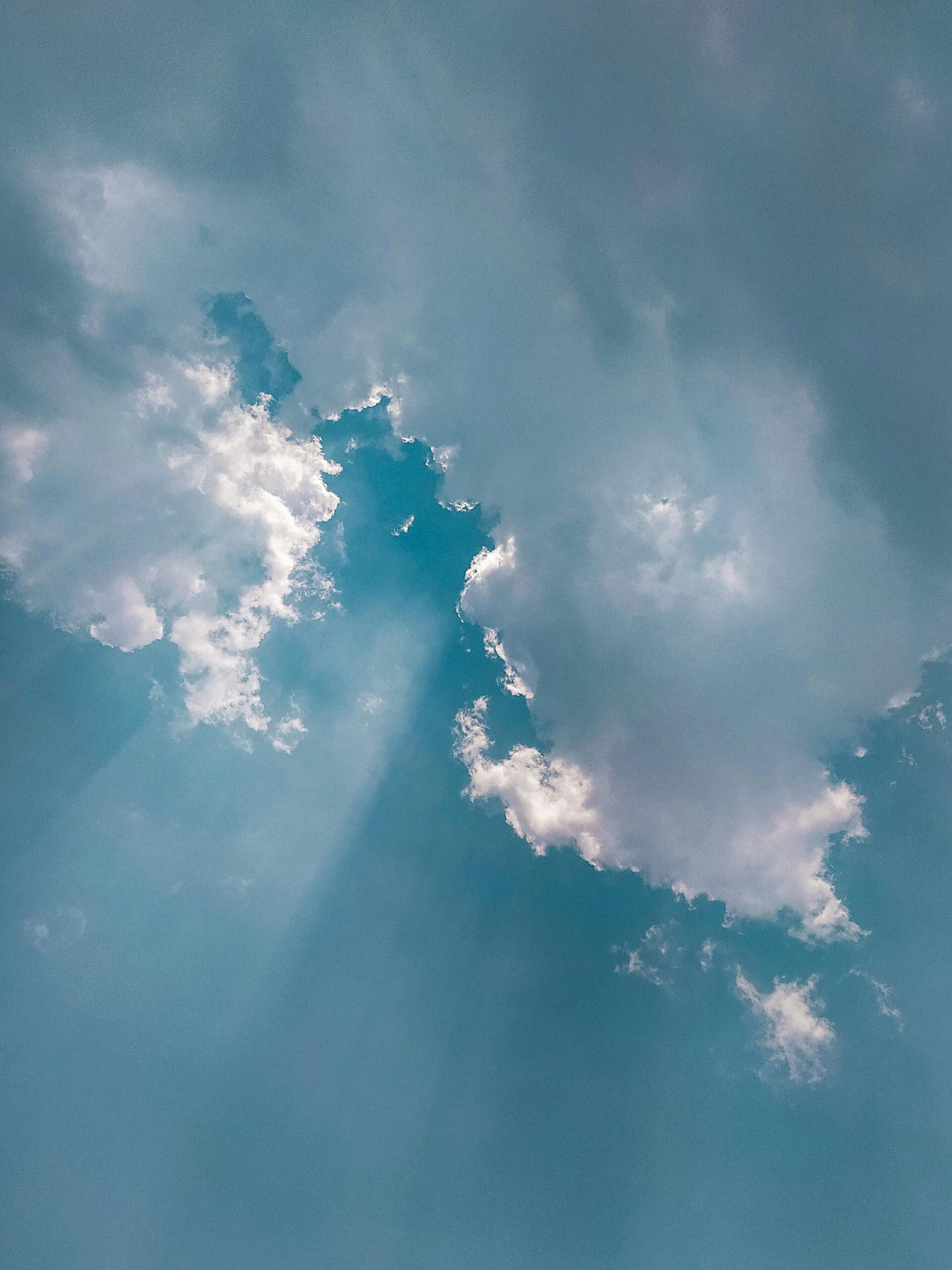 Stunning cumulus clouds in a vibrant blue sky with sunrays streaming through for a serene atmosphere.